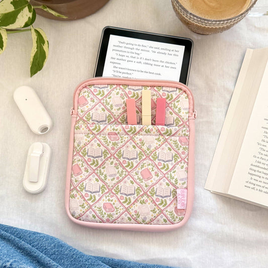 Pink case with small items on a table with a plant, coffee, and book.