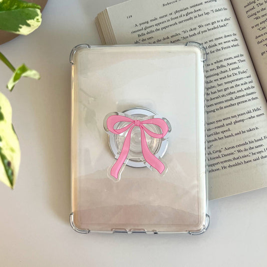Phone case with pink bow design on a book next to a plant