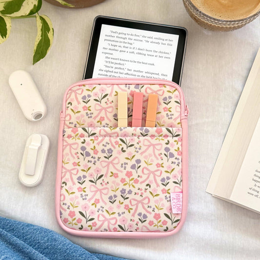 Floral-patterned pink case on a table with a tablet, coffee, and book.